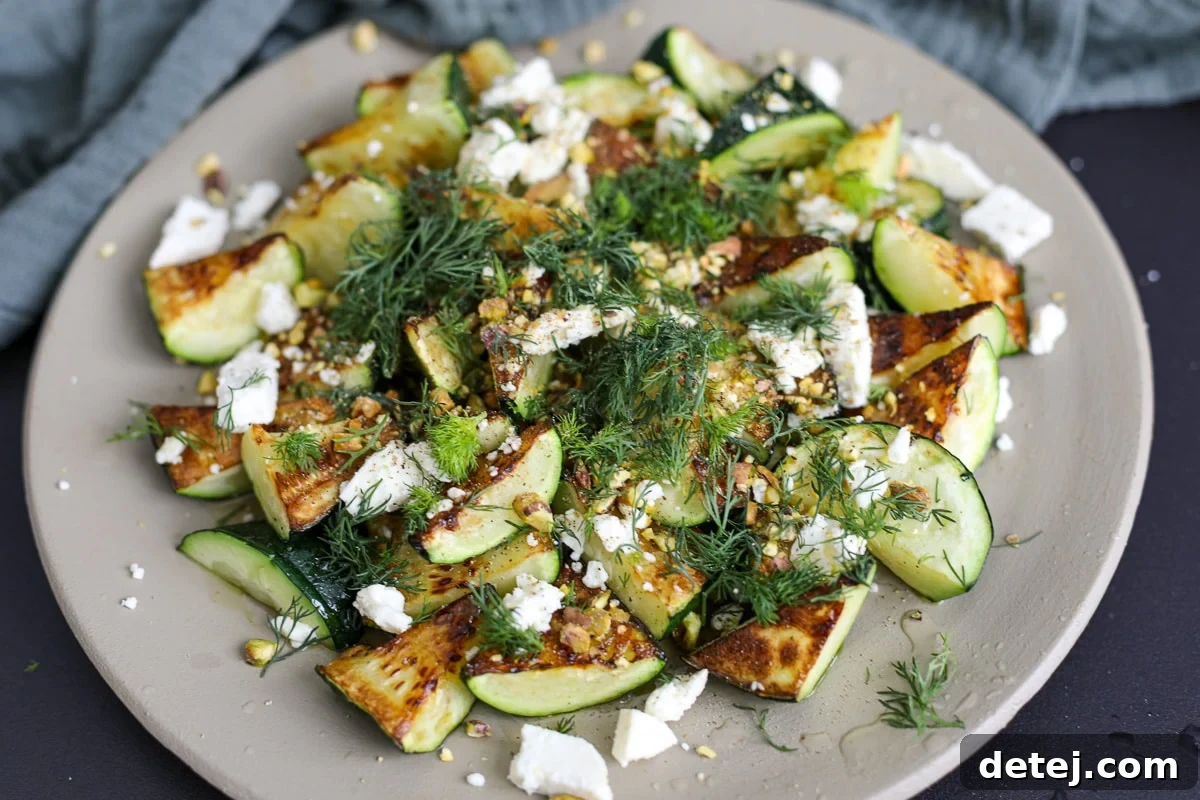 Sautéed zucchini served on a white plate, artfully topped with feta, pistachios, honey, and dill, showcasing its freshness and vibrant colors.