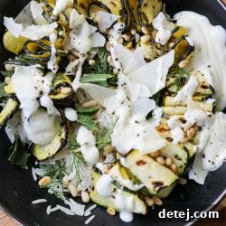 Overhead shot of a vibrant Grilled Zucchini Ribbon Bowl with all toppings, including fresh herbs, parmesan, and a drizzle of Greek yogurt sauce.