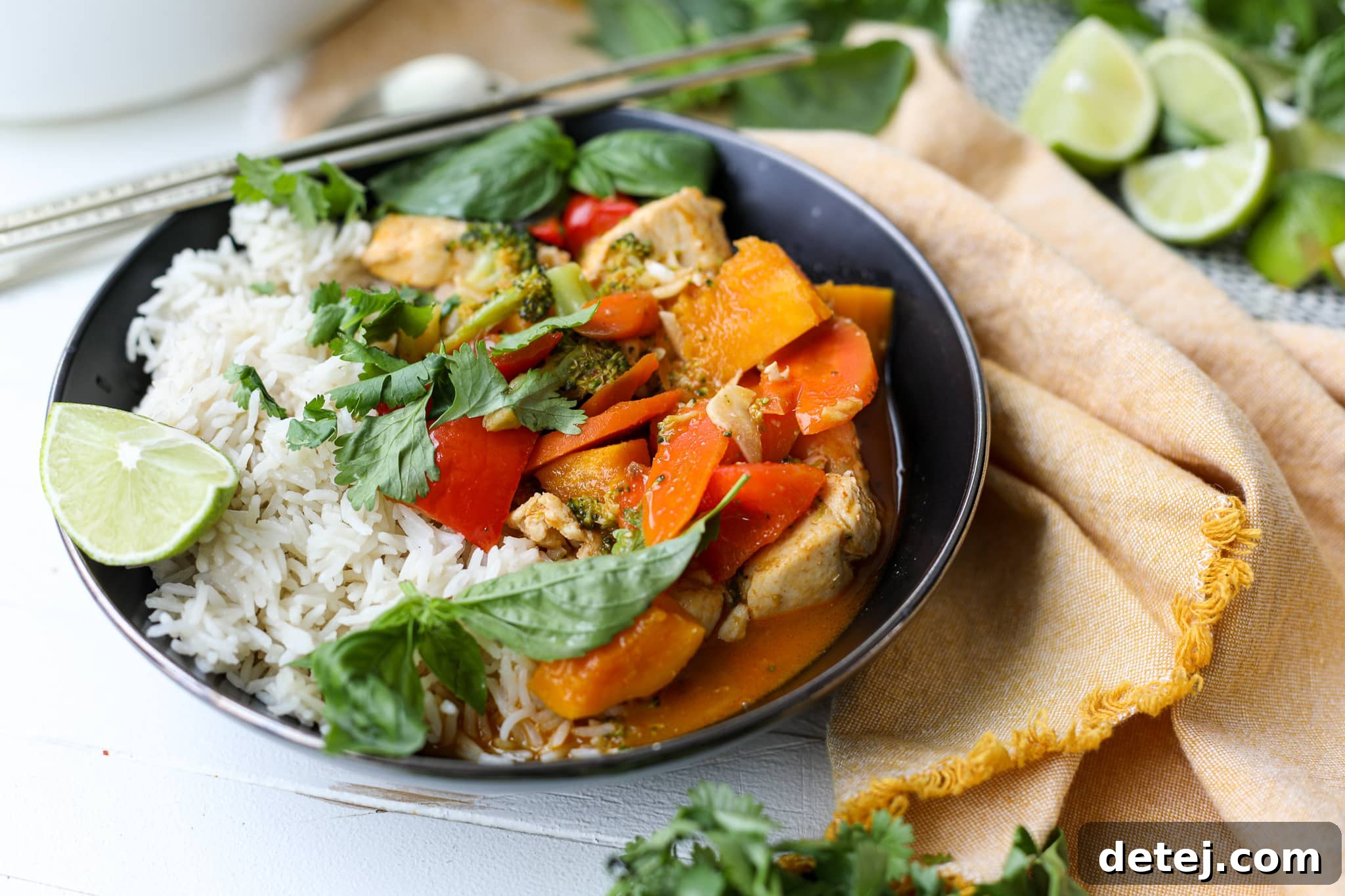 A bowl of Thai Red Curry Chicken and Vegetables, garnished with fresh herbs and lime.