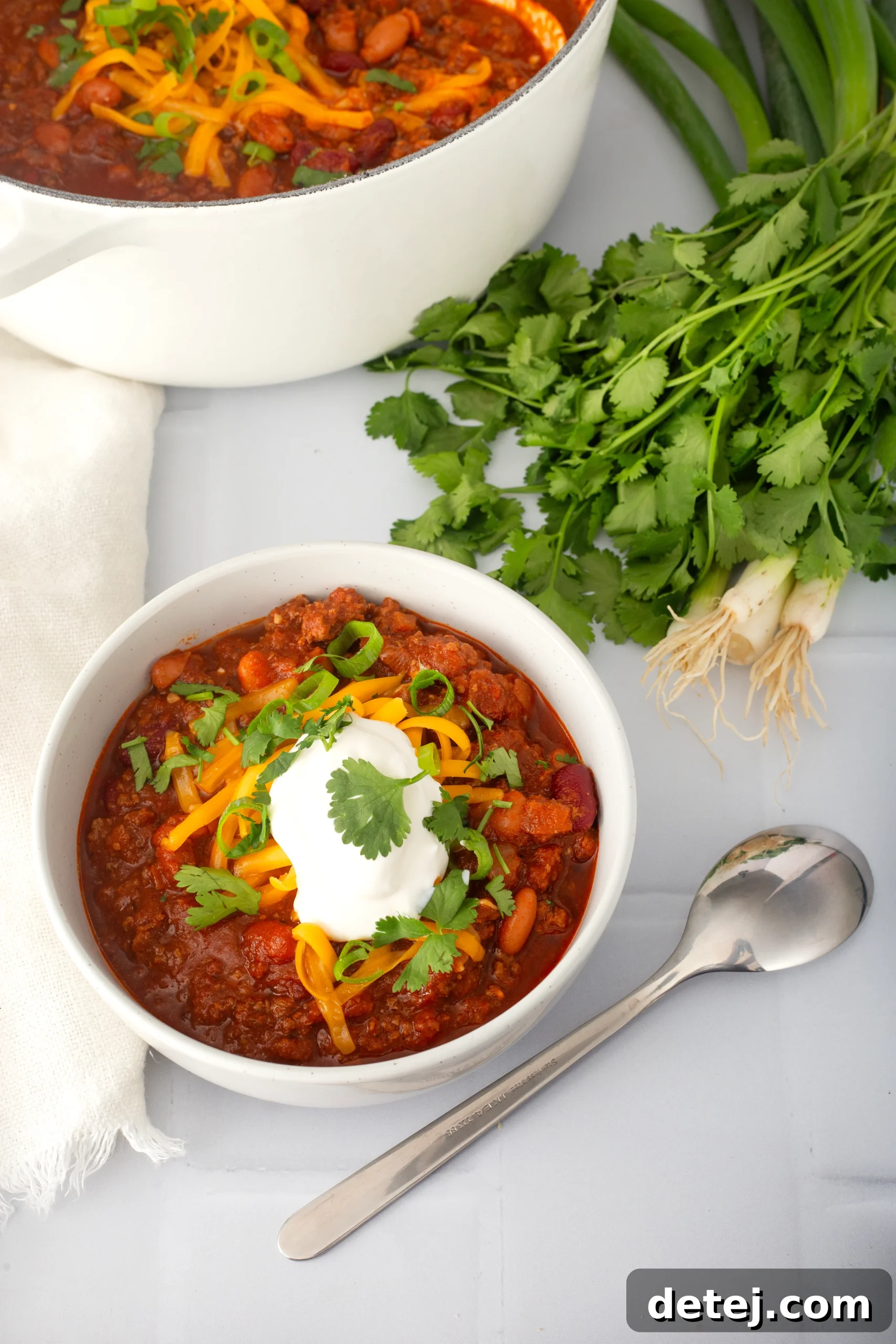 A wooden spoon actively stirring vibrant chili powder and concentrated tomato paste into browned ground meat in a large pot, creating a rich flavor base.
