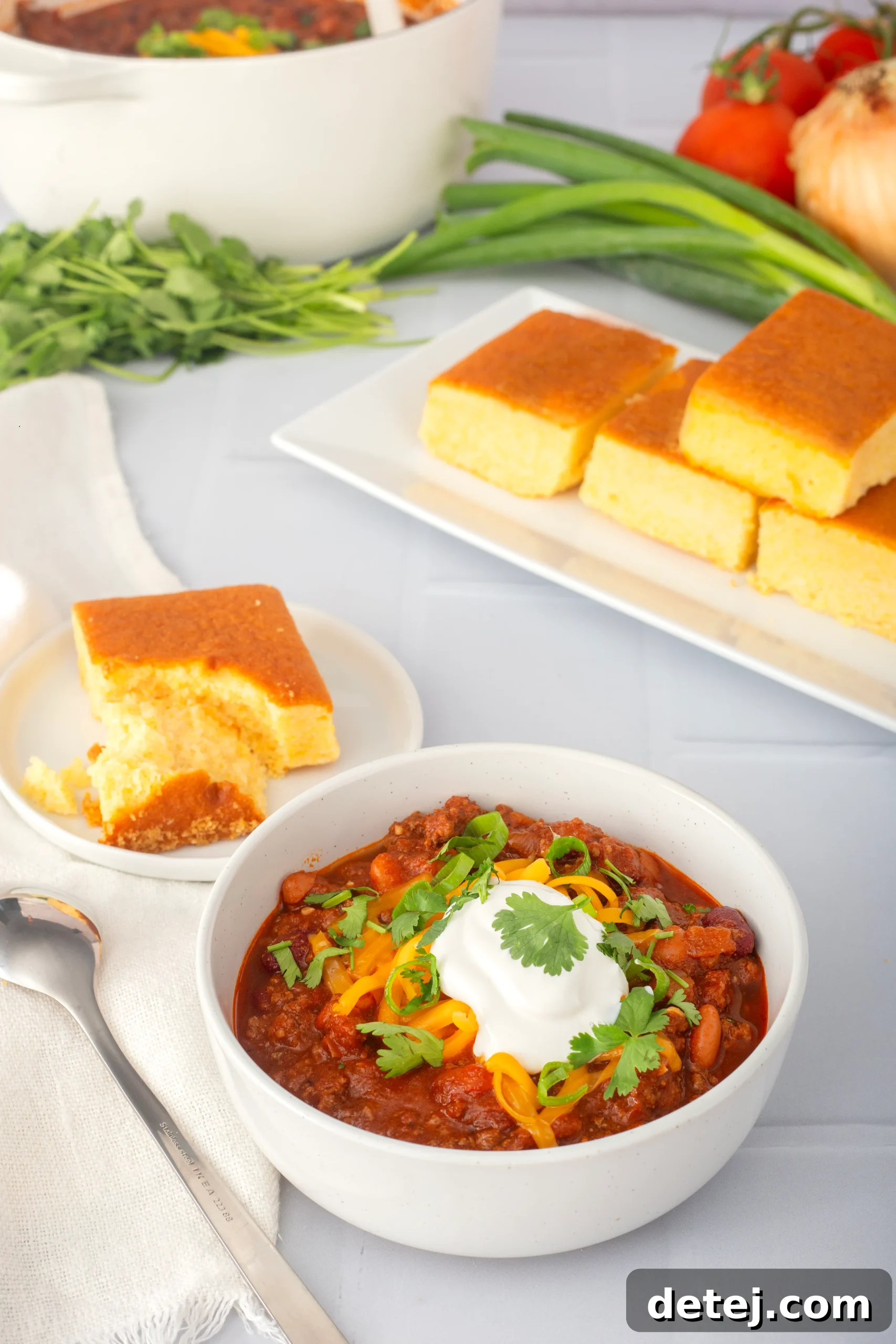 A beautifully presented bowl of homemade stovetop chili, generously topped with shredded cheddar cheese, a dollop of sour cream, and fresh green onions and cilantro, ready to be savored.