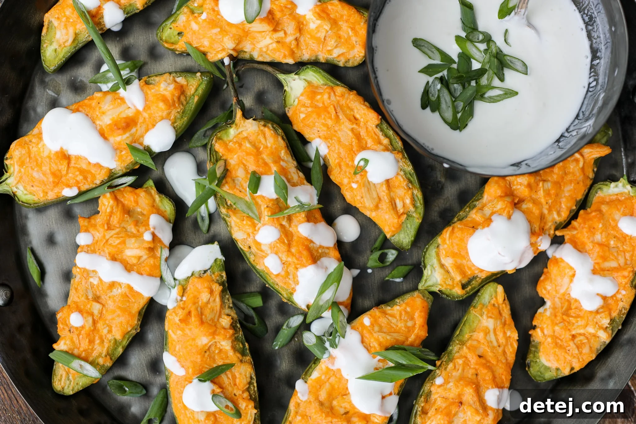 A vibrant platter of freshly baked Buffalo Chicken Jalapeno Poppers, garnished with green onions and a drizzle of creamy lime crema, ready to be served.