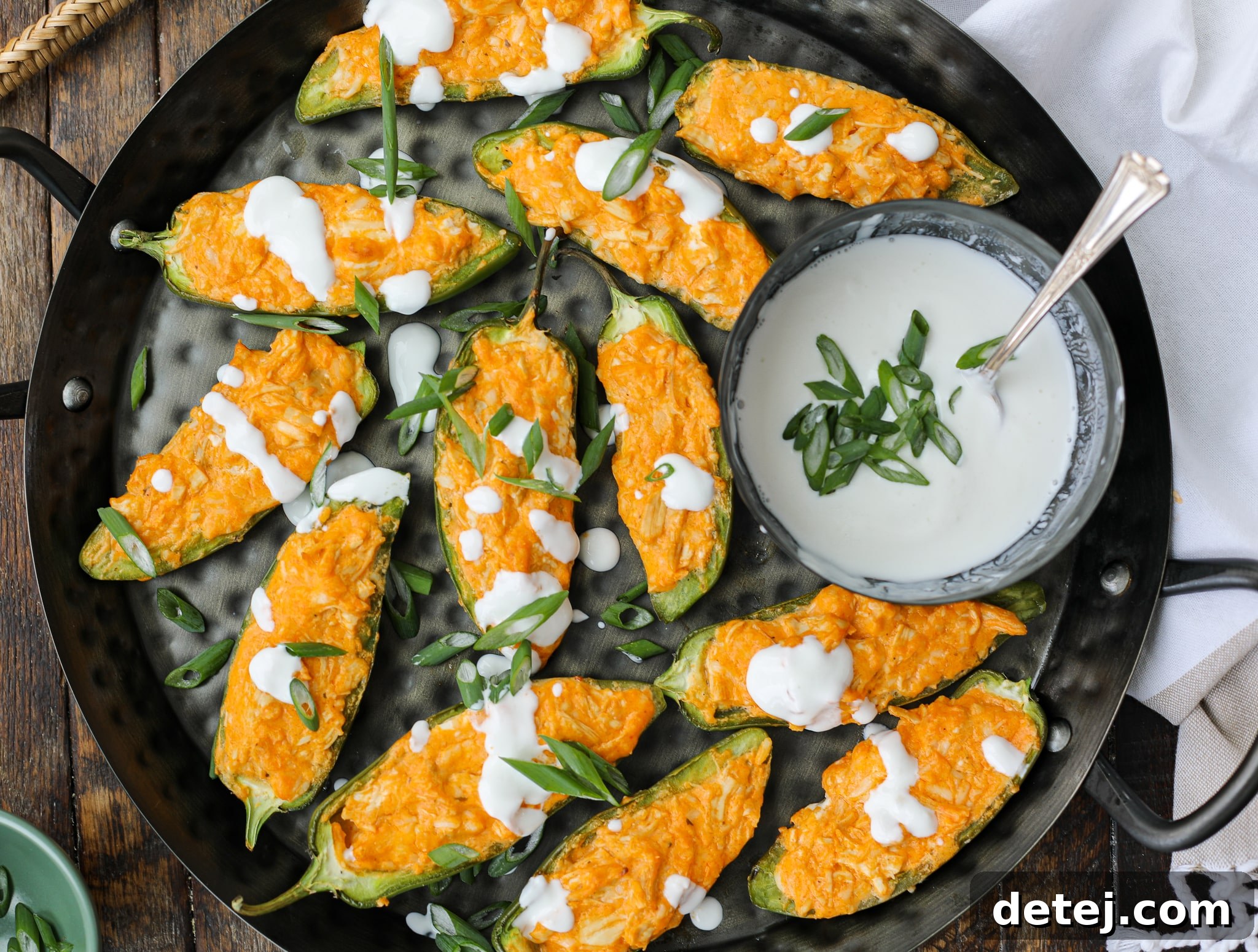 A beautifully presented serving platter of golden-brown Buffalo Chicken Jalapeno Poppers, generously garnished with chopped green onions and a final drizzle of fresh lime crema, inviting guests to indulge.