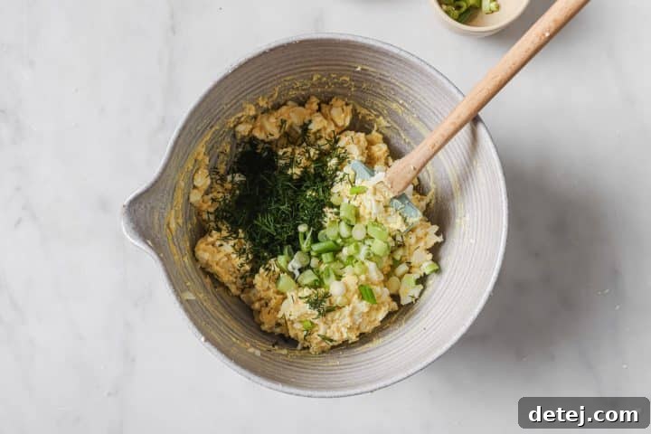 Freshly chopped dill and green onions added to the creamy egg salad base in a bowl, ready for final mixing.