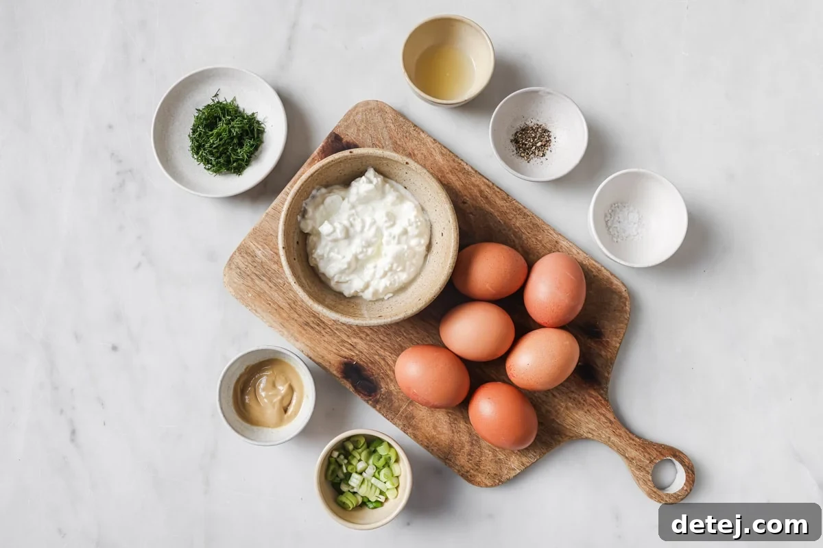A collection of fresh ingredients laid out, including hard-boiled eggs, cottage cheese, Dijon mustard, lemon, and fresh dill, ready for making cottage cheese egg salad.