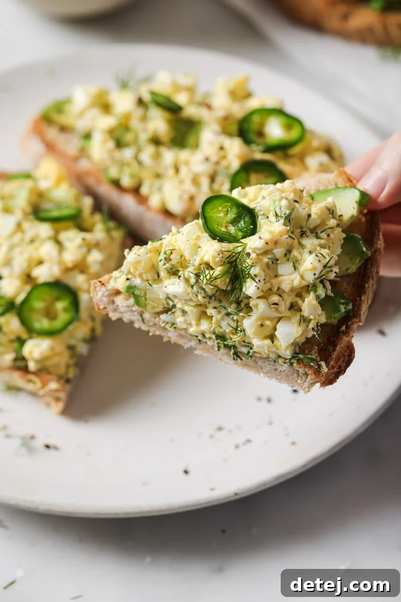 A hand holding a piece of toasted bread generously topped with cottage cheese egg salad, ready to be enjoyed as a healthy lunch.
