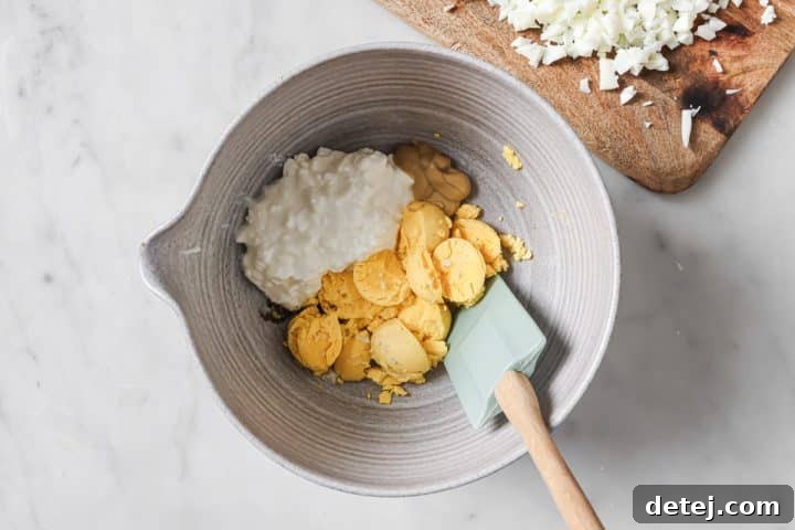Egg yolks combined with cottage cheese, Dijon mustard, and lemon juice in a mixing bowl, ready to be mashed.