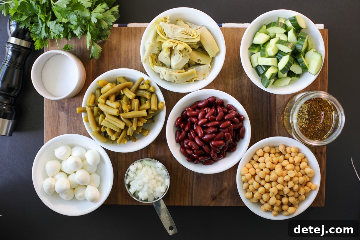 Close-up view of fresh ingredients laid out, including canned beans, cucumber, onion, artichoke hearts, and mozzarella, ready for making three bean salad.