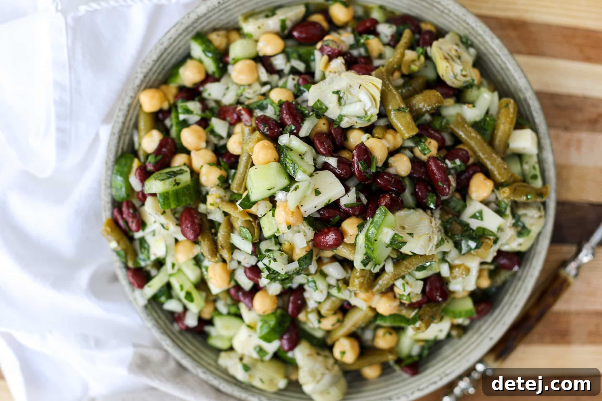 A large mixing bowl filled with vibrant three bean salad ingredients, tossed with dressing.