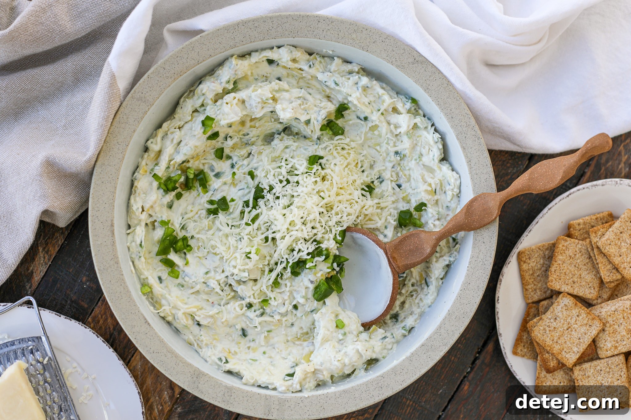 Close-up of creamy Healthyish Jalapeno Artichoke Cheese Dip in a bowl with a spoon.