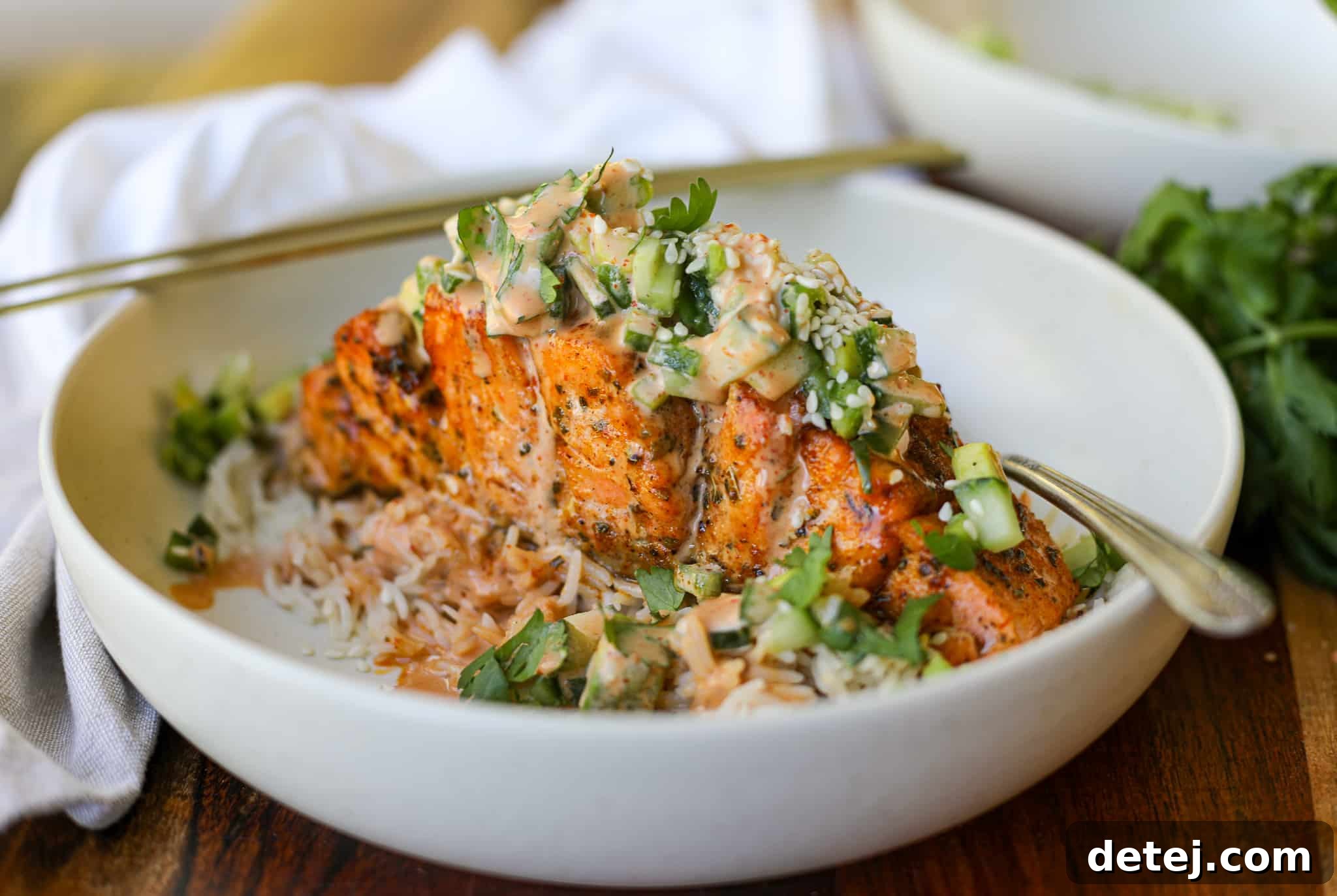 Crispy Air Fryer Spicy Hasselback Salmon garnished with fresh salad and spicy sauce, served in a bowl.