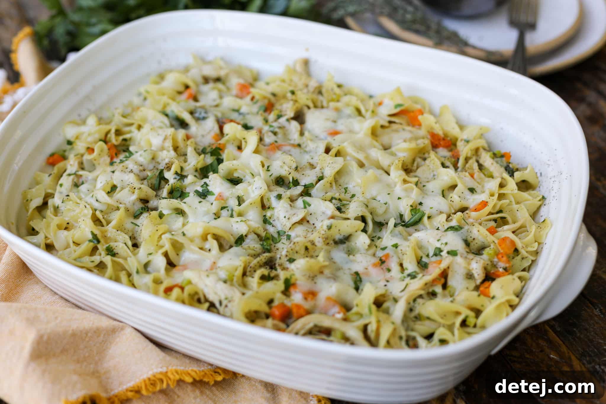 A golden-brown Chicken Noodle Soup Pasta Bake, bubbling hot, in a white baking dish on a wooden surface.