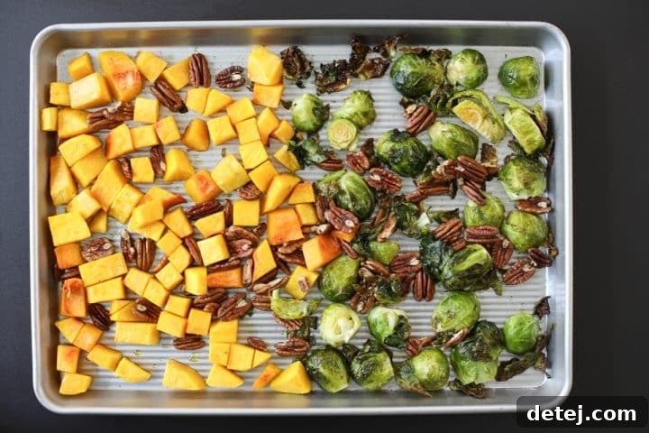 Perfectly roasted butternut squash, Brussels sprouts, and toasted pecans on a sheet tray after being removed from the oven.