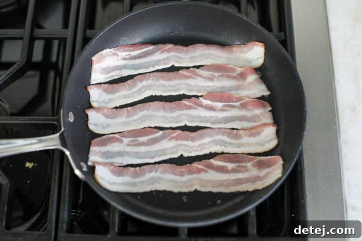 Thick-cut bacon sizzling in a pan, halfway through cooking.