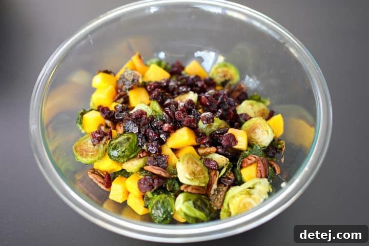 A large mixing bowl filled with roasted Brussels sprouts, butternut squash, pecans, and cranberries, ready to be dressed.