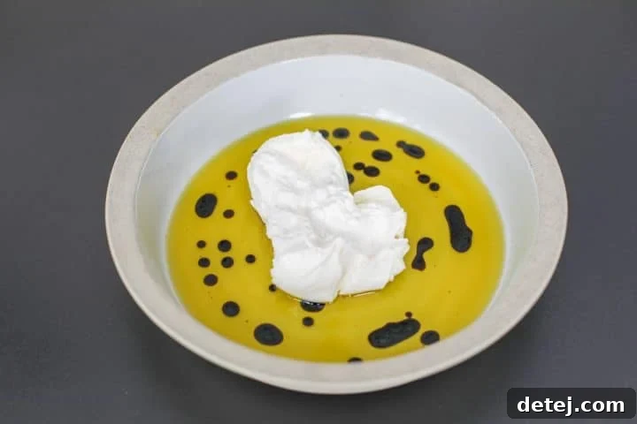 Luscious Burrata Bruschetta Dip 6 A serving bowl with extra virgin olive oil and balsamic glaze, with a plump ball of burrata cheese carefully placed in the center, ready to be opened.