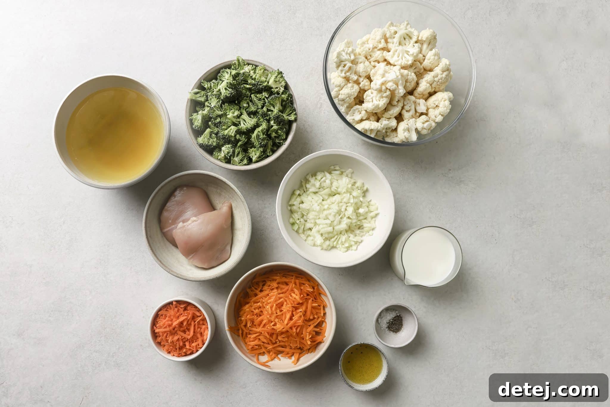 Various fresh ingredients for making a healthy broccoli cheddar soup laid out neatly on a wooden cutting board, including broccoli florets, carrots, onions, and chicken.