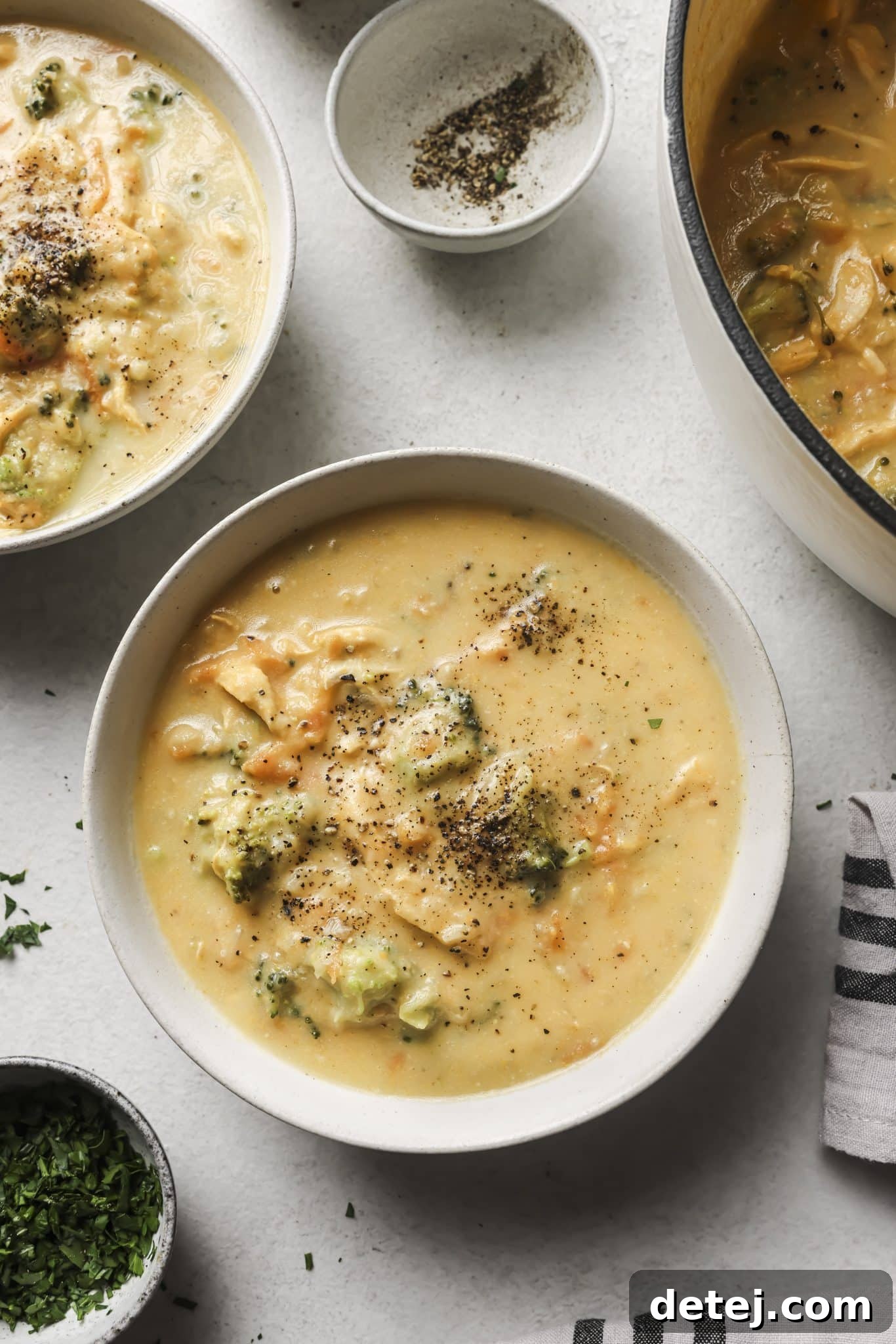 Two cozy bowls of healthy chicken broccoli cheddar soup, garnished with parsley, on a white countertop, emphasizing comfort and warmth.