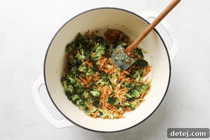 Close-up of diced onions, chopped broccoli, and grated carrots sautéing in a soup pot, capturing vibrant colors and textures.