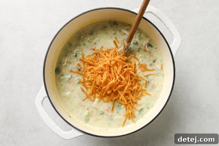 Freshly grated cheddar cheese being stirred into the simmering soup in a pot, creating a creamy texture.