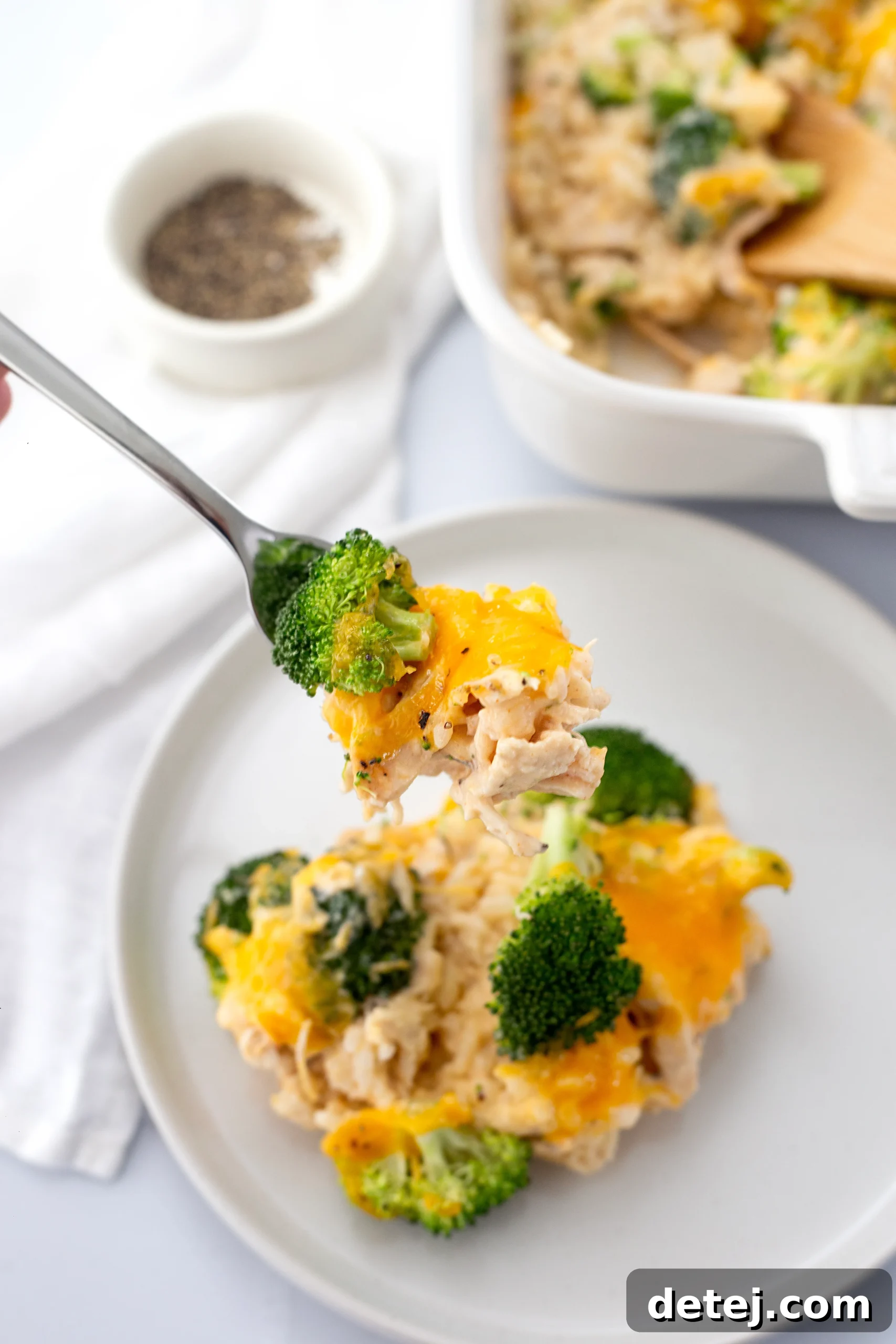 A close-up of a serving of cheesy chicken broccoli rice casserole on a plate, garnished with fresh parsley.