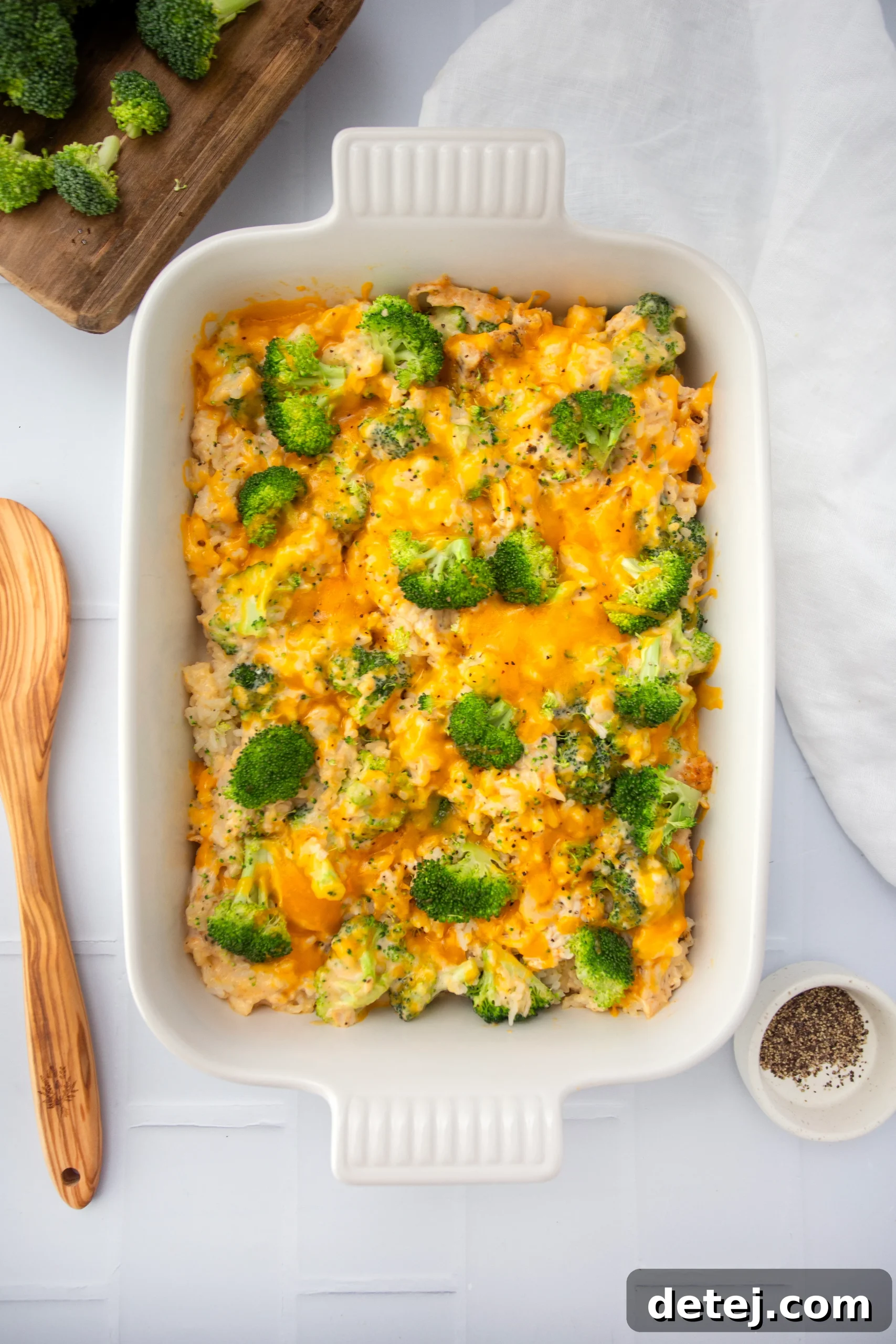 A serving spoon lifting a portion of cheesy chicken broccoli rice casserole from a white baking dish, showcasing the creamy texture and melted cheese.
