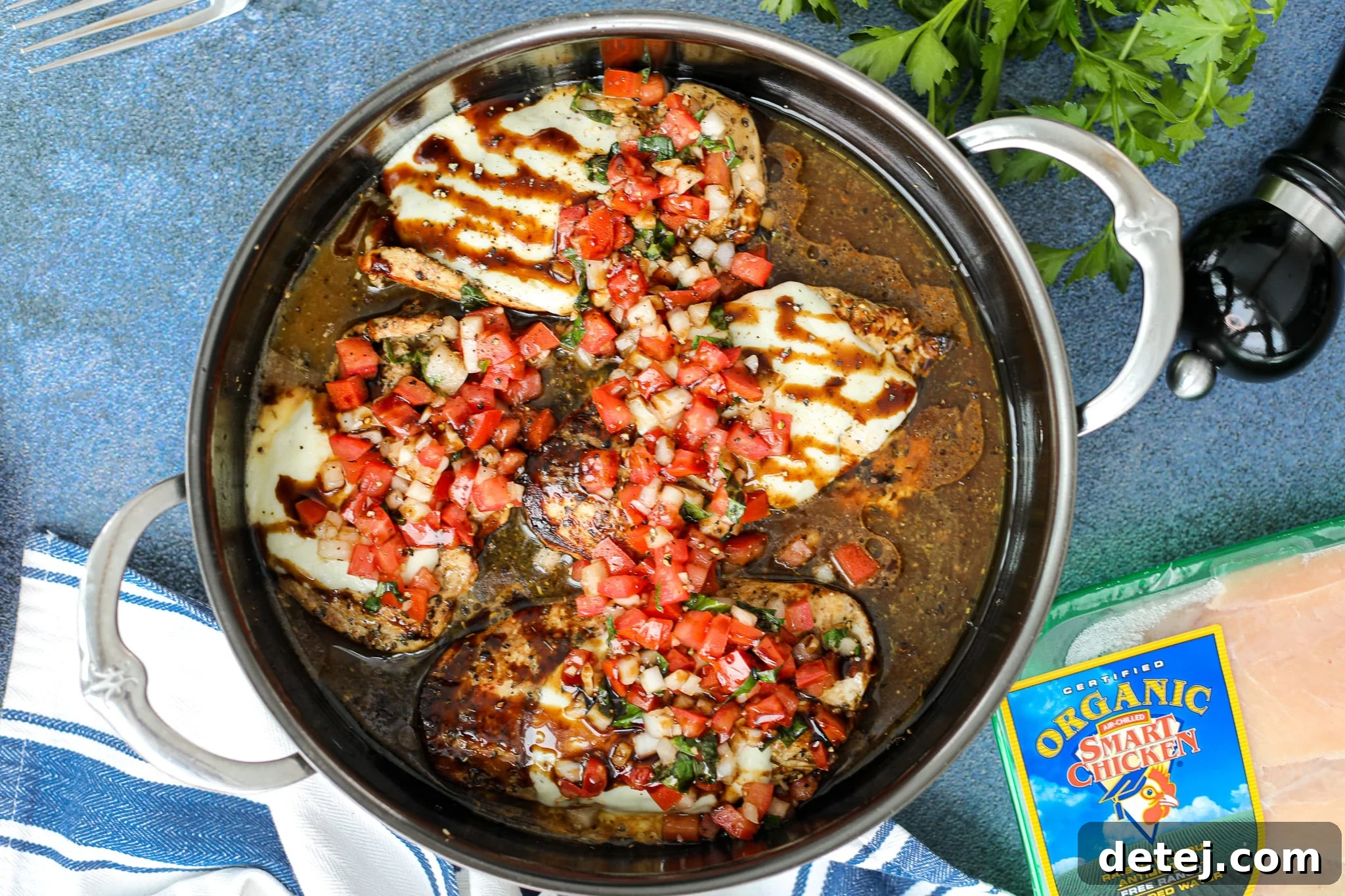 A close-up of a chicken cutlet topped with melted mozzarella, diced tomatoes, basil, and a drizzle of balsamic glaze.