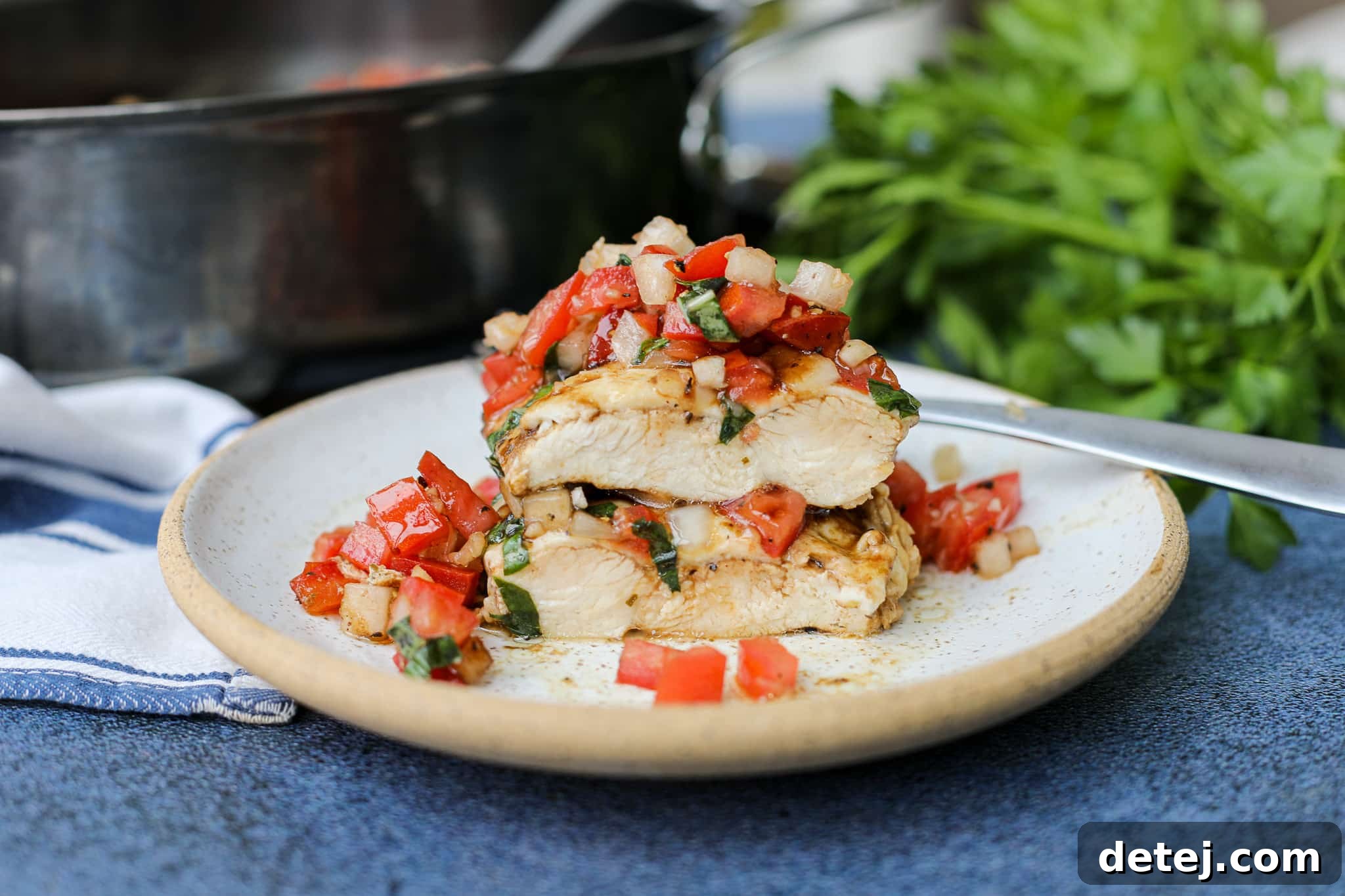 Four servings of bruschetta chicken on white plates, garnished with fresh basil leaves.
