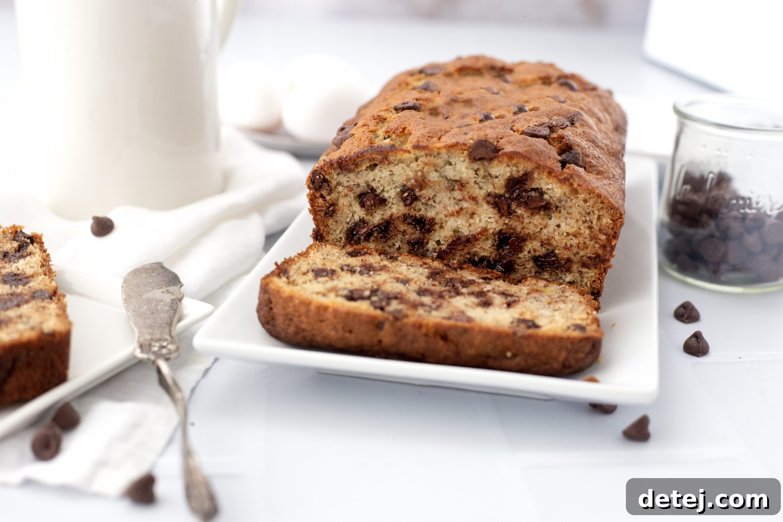 Close-up of a hand reaching for a slice of chocolate chip banana bread.