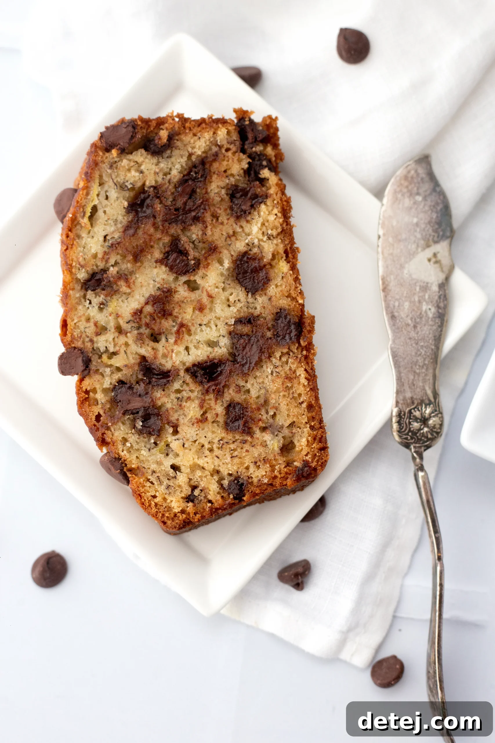 A slice of chocolate chip banana bread drizzled with chocolate sauce, on a plate.