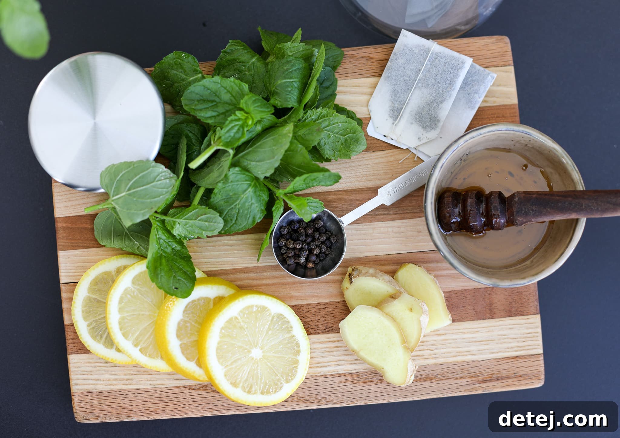 Digestive Harmony Tea 3 Ingredients for Healthyish Digestion Tea, including fresh ginger, lemon, mint, and peppercorns, laid out on a surface.