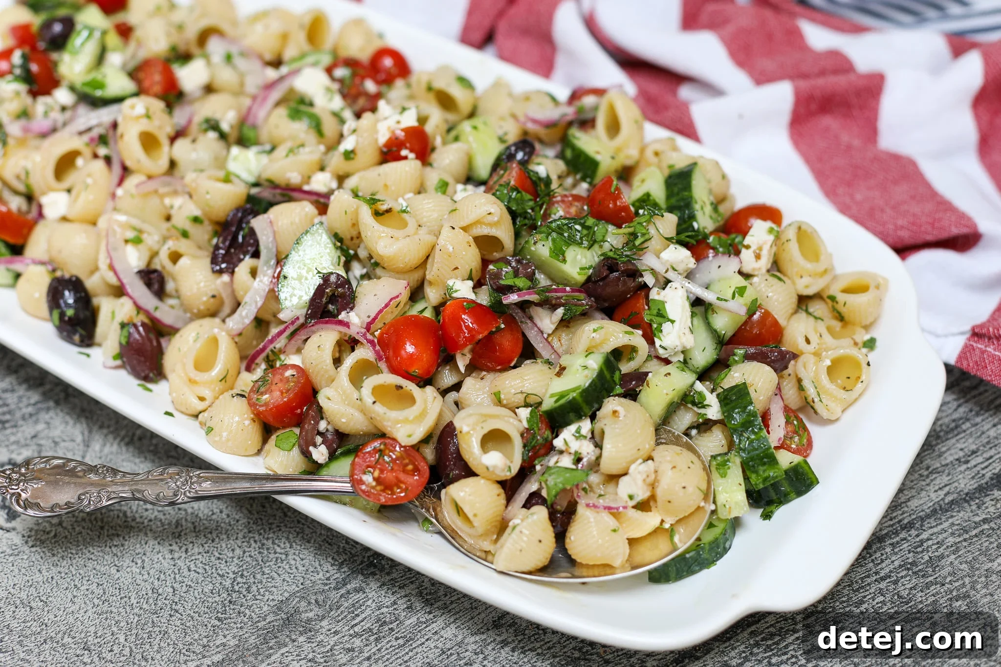 Vibrant and fresh Greek Pasta Salad with pasta, cucumber, tomatoes, feta, and olives in a large white bowl, garnished with fresh dill.