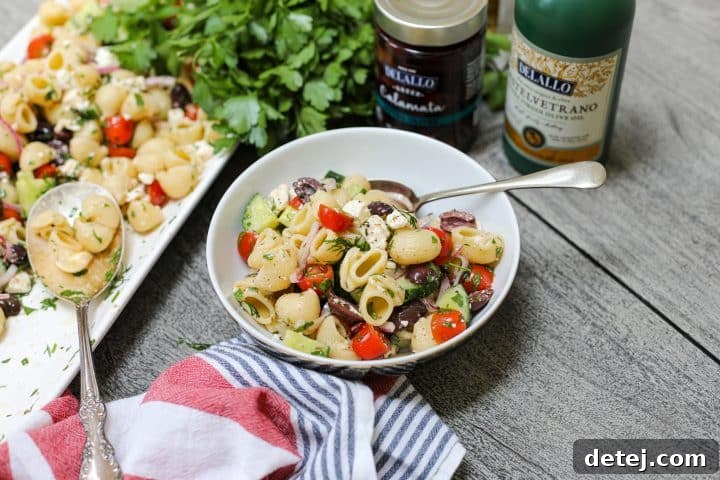 Large serving bowl of Greek Pasta Salad, beautifully garnished with fresh herbs and a drizzle of olive oil, ready to serve at a party.