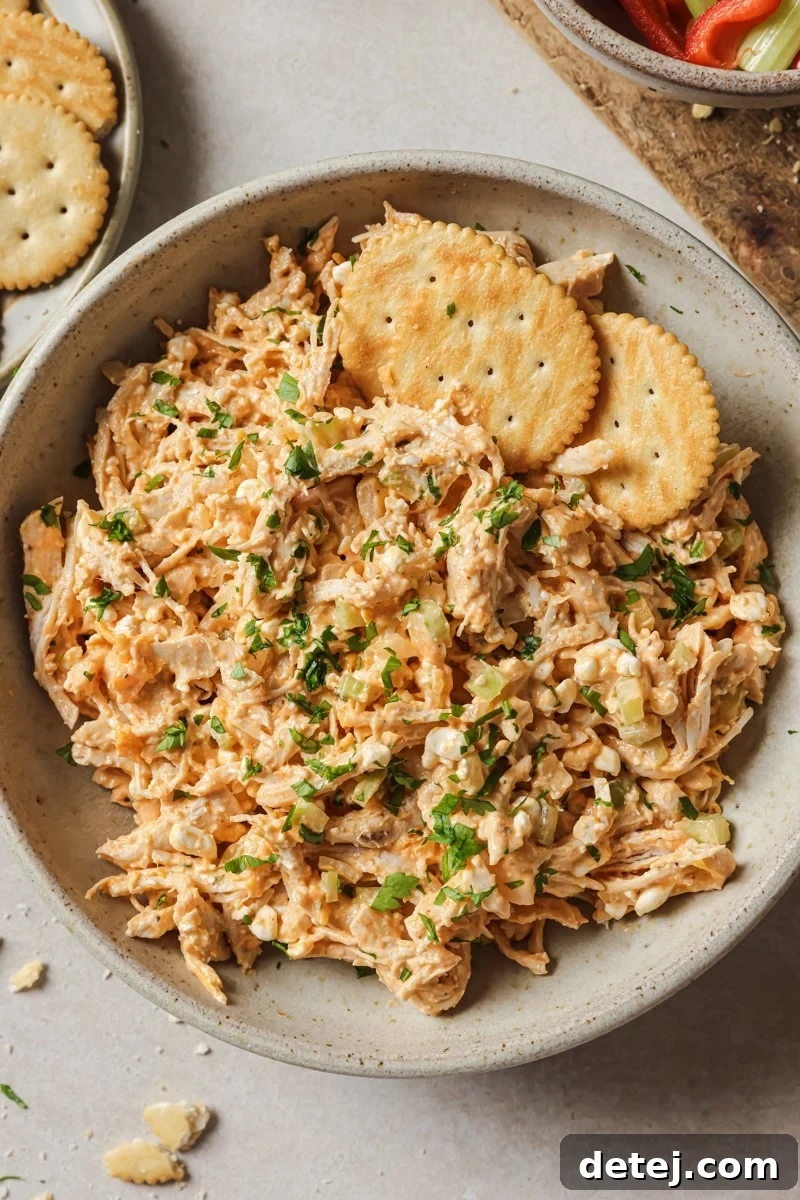 A bowl of vibrant Buffalo Chicken Salad, ready to be enjoyed with a side of fresh vegetables and crackers.