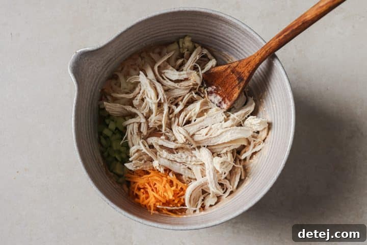 Shredded chicken being added to the prepared buffalo dressing in a mixing bowl.