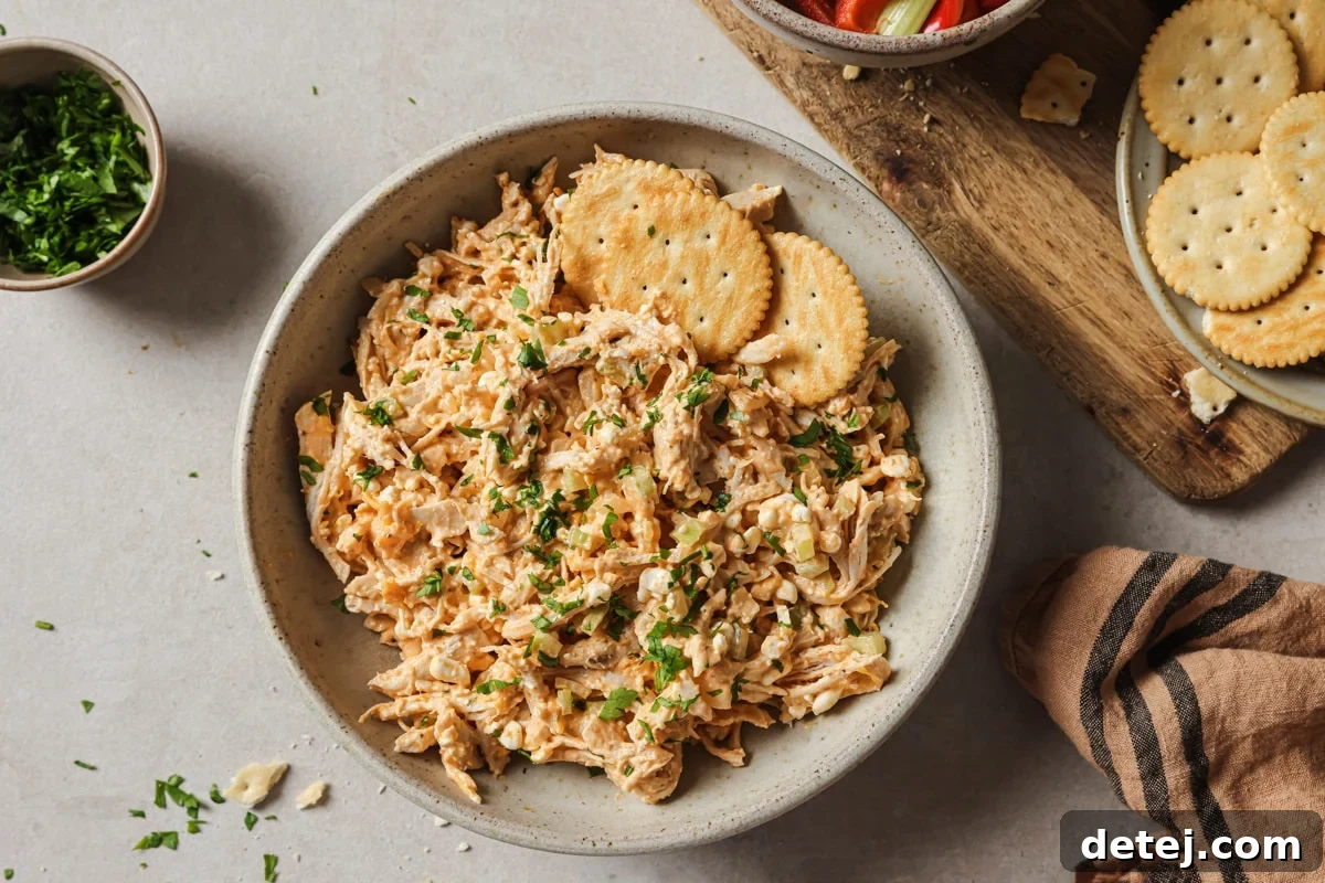 A serving of buffalo chicken salad in a bowl, accompanied by crunchy crackers and fresh celery sticks.