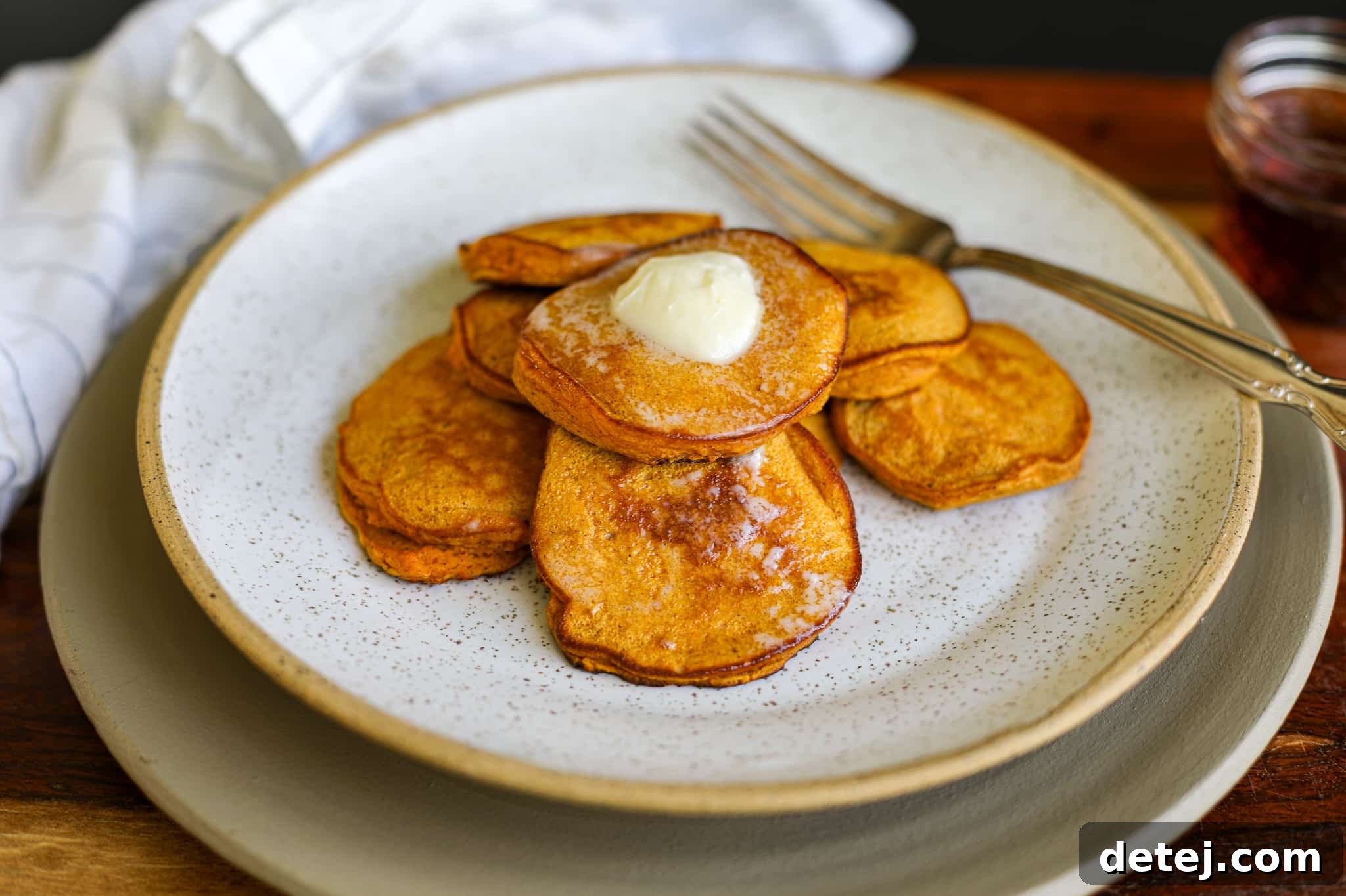 Side angle view of stacked Healthy Sweet Potato Pancakes, with syrup drizzled.