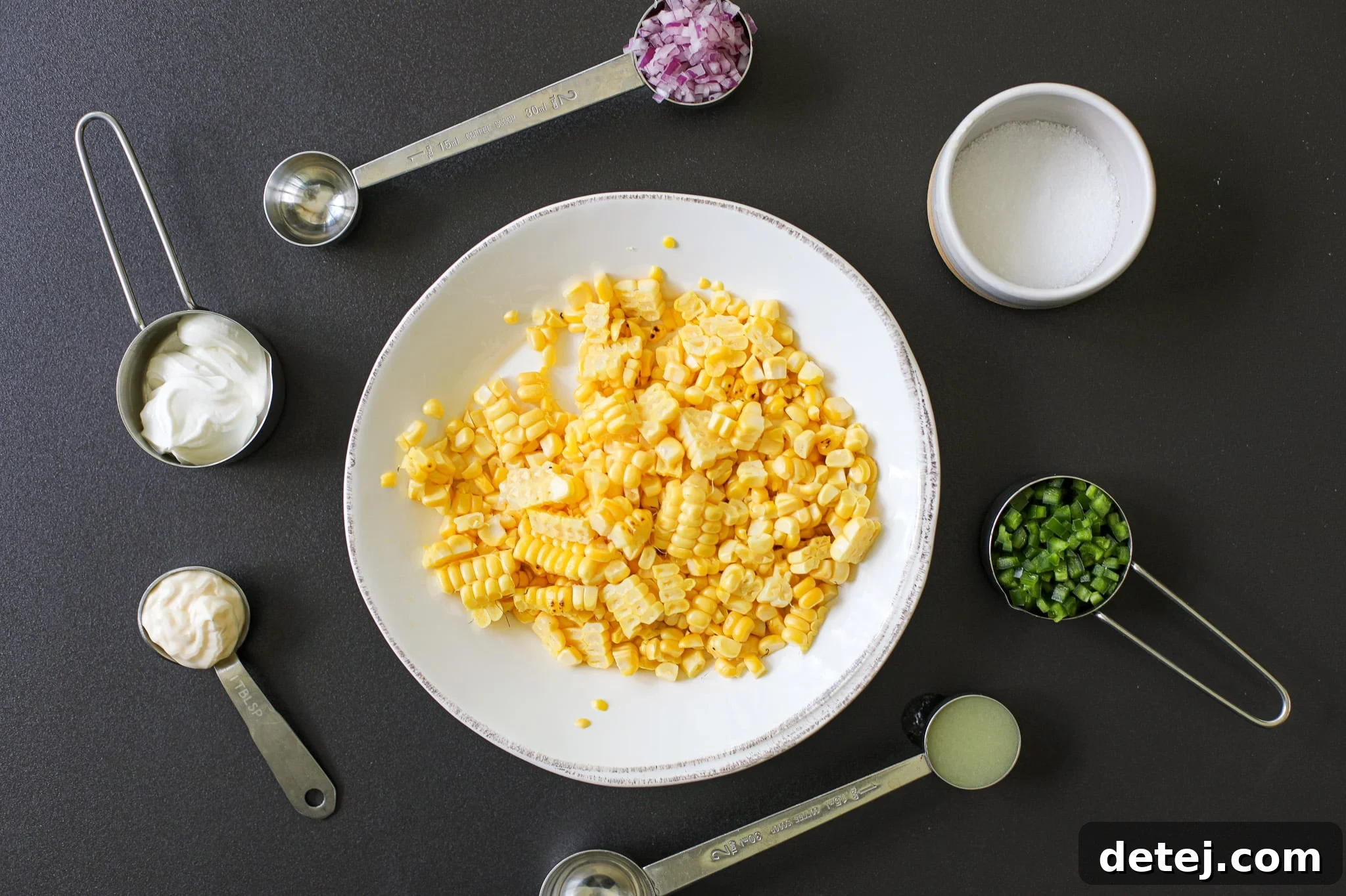 Fresh ingredients laid out for Creamy Corn Salsa: grilled corn, jalapeno, red onion, lime, sour cream, mayonnaise, and cilantro.