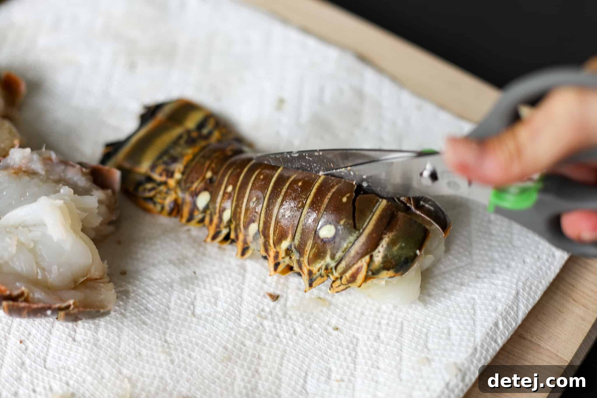 Using kitchen shears to carefully cut through the top shell of the lobster tail.