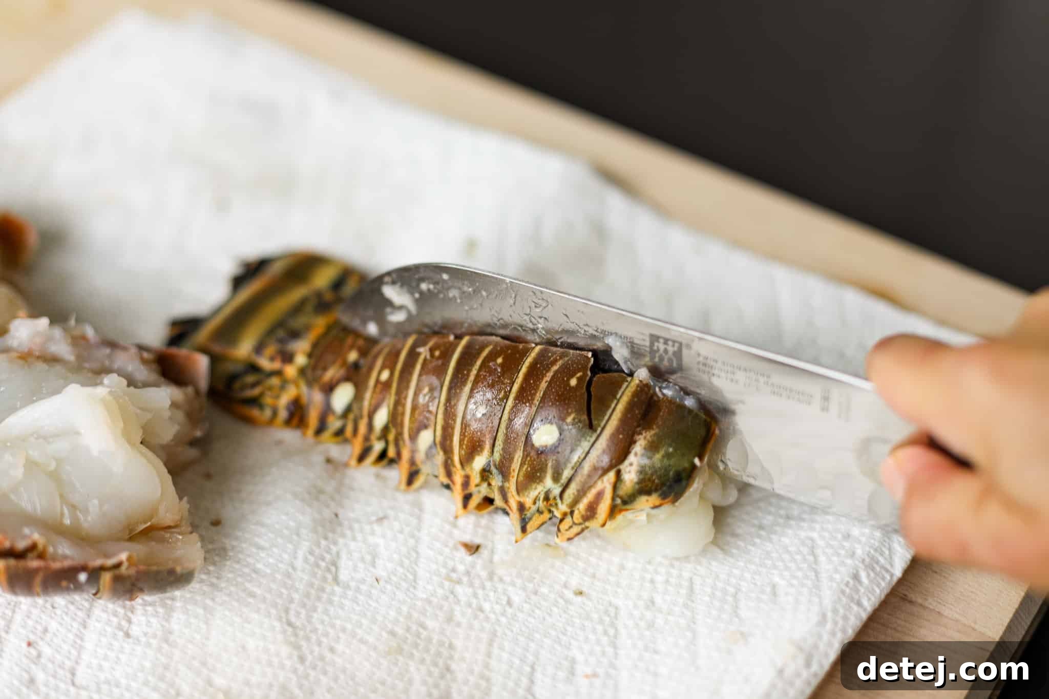 A sharp knife slicing through the lobster meat to butterfly the tail.