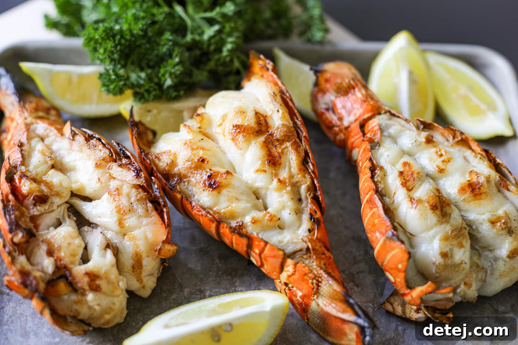 A stunning beauty shot of perfectly grilled lobster tails on a serving platter, garnished with fresh herbs and lemon wedges.