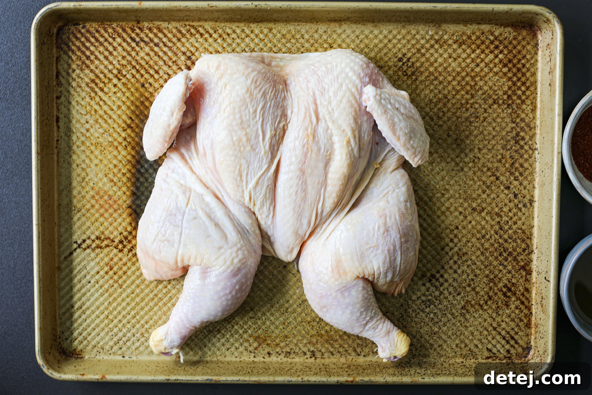 Seasoned spatchcocked whole chicken on a baking sheet, ready for the grill.