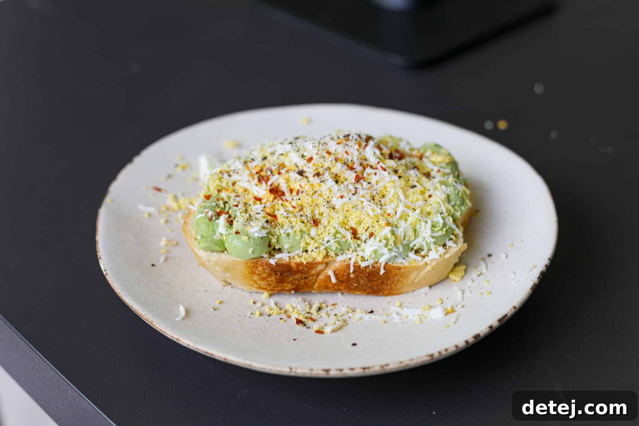 Side view of a perfectly assembled Grated Egg Avocado Toast, showing the layers of crispy sourdough, piped avocado cottage cheese mousse, and a generous topping of grated hard-boiled egg.