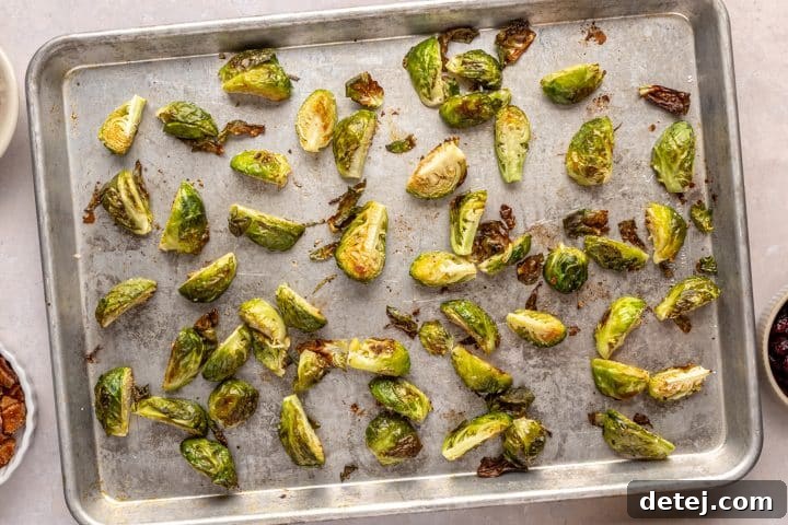 Prepared Brussels sprouts tossed with oil and seasoning on a baking tray.