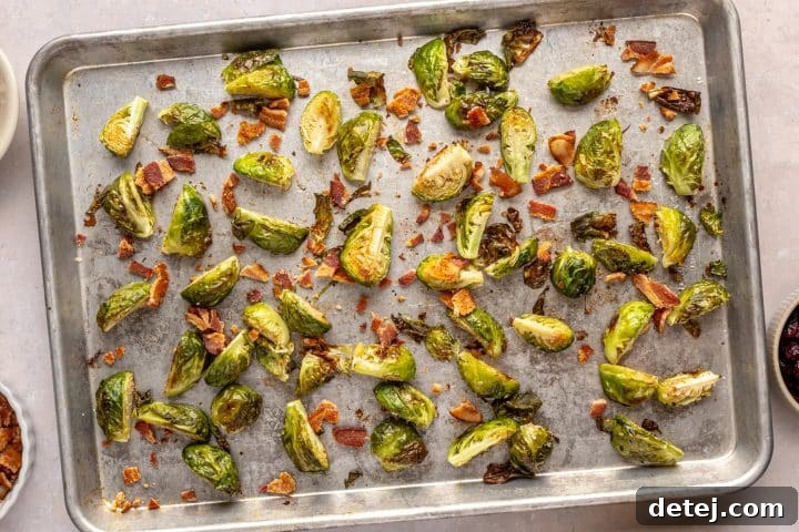 Roasted Brussels sprouts on a baking tray with crumbled bacon added.