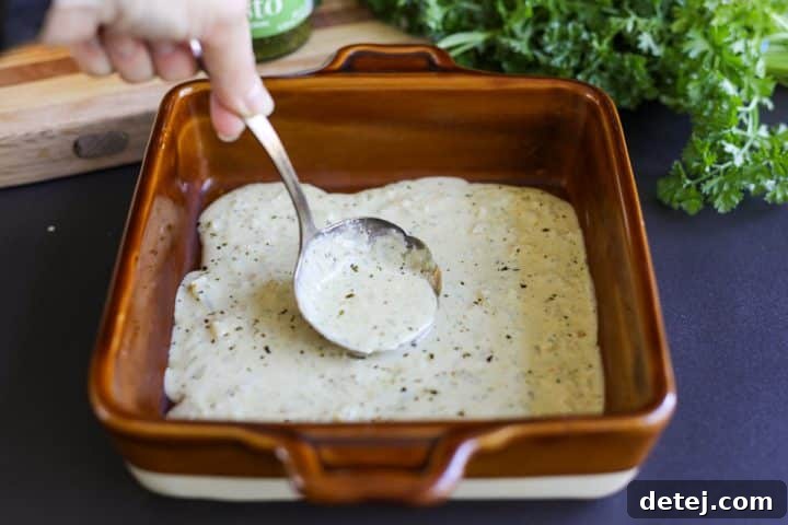 spreading out creamy pesto sauce on the bottom of a ceramic baking dish.