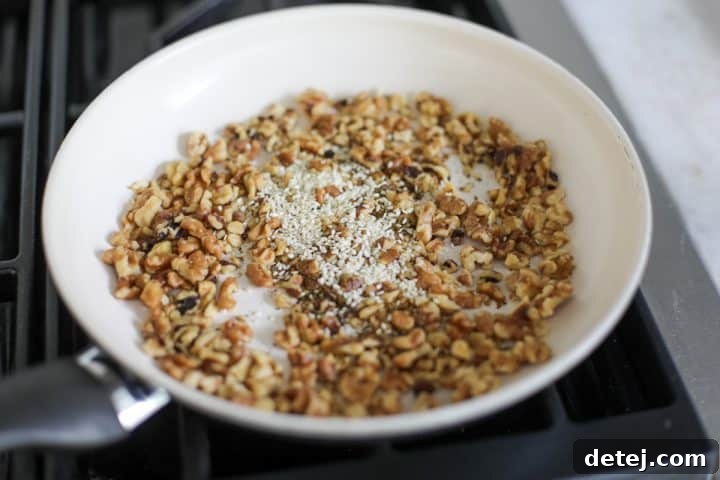 Walnut pieces in a pan, now with za'atar, kosher salt, and sesame seeds added.
