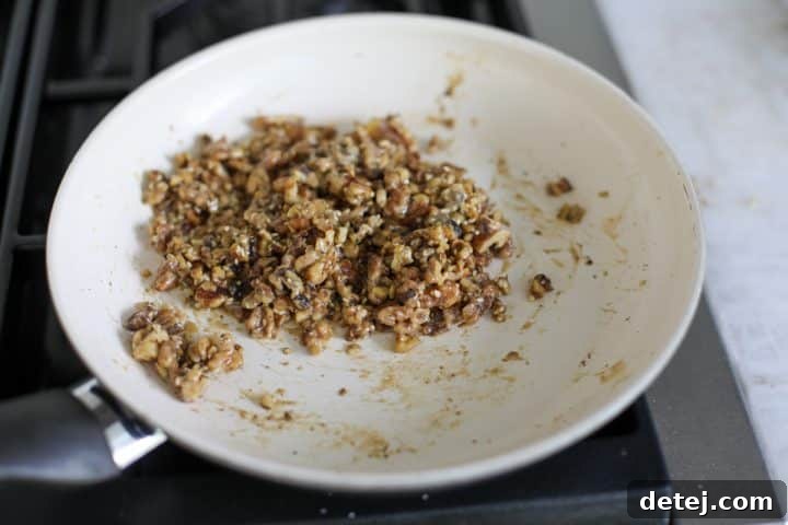 The walnuts are now coated in maple syrup and tahini, creating a sticky mixture.