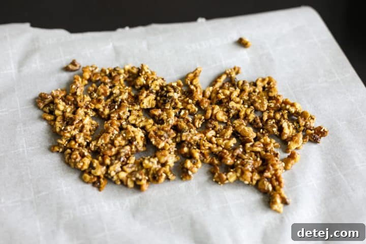 Sticky walnuts spread out on parchment paper to cool and prevent sticking.
