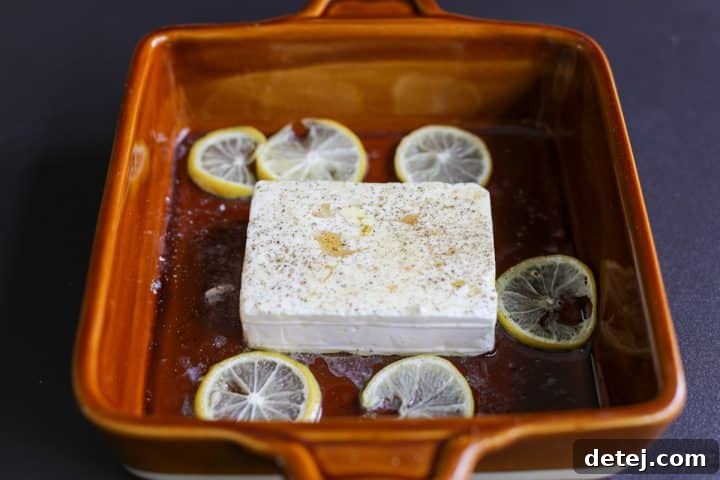 The baked feta is removed from the oven, brushed with warmed honey, and sprinkled with cracked black pepper before broiling.
